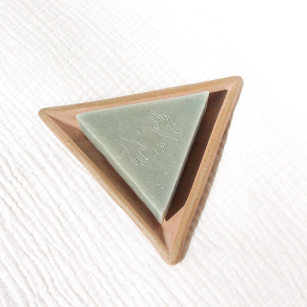 A triangular soap on a triangular soap dish against textured linen