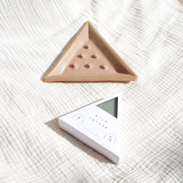 A triangular ceramic soap dish and triangle soap against textured linen