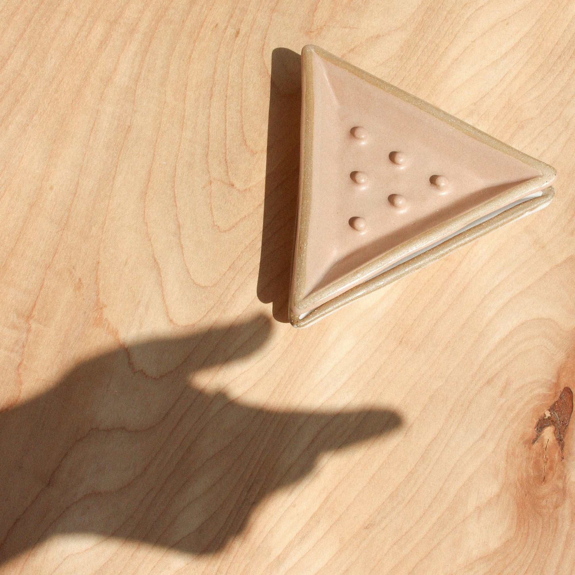 Two triangular ceramic soap dishes and a shadow hand against wood grain