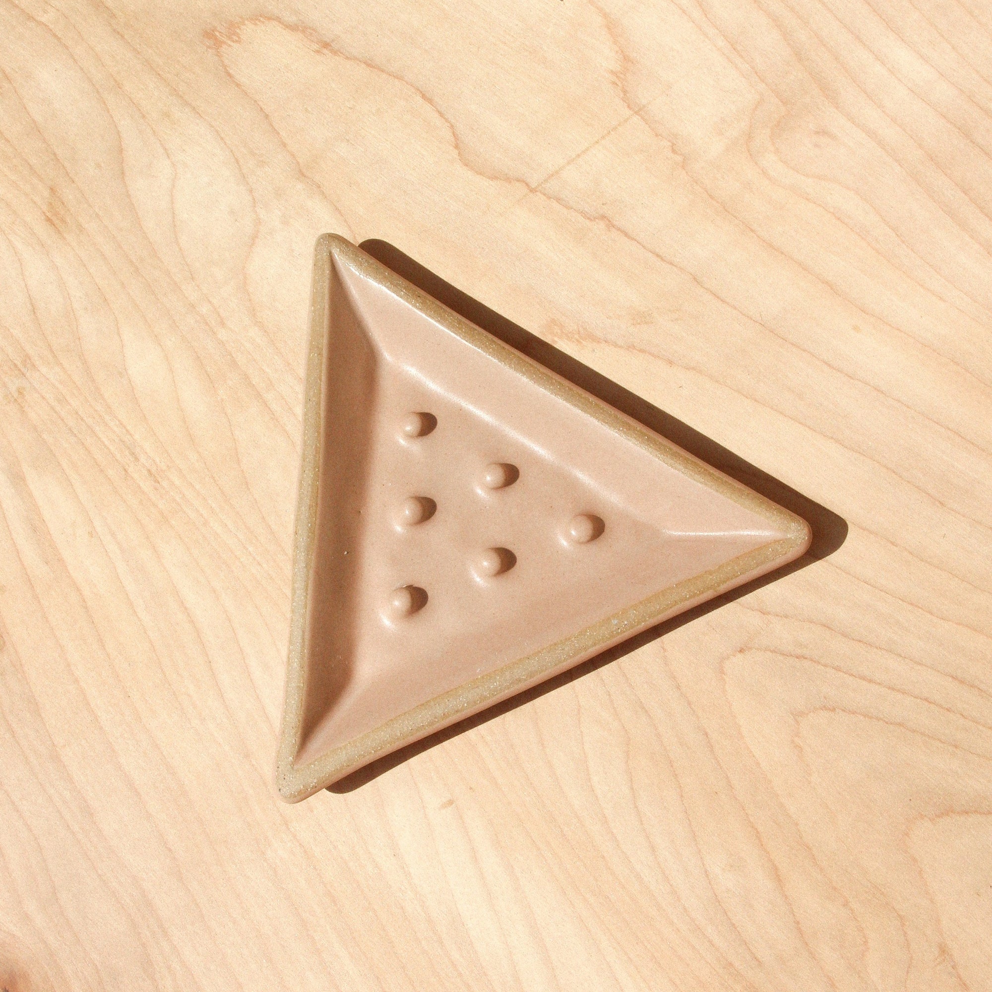 A triangular ceramic soap dish against wood grain