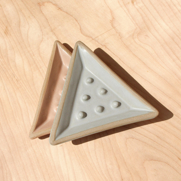 Two triangular ceramic soap dishes against wood grain