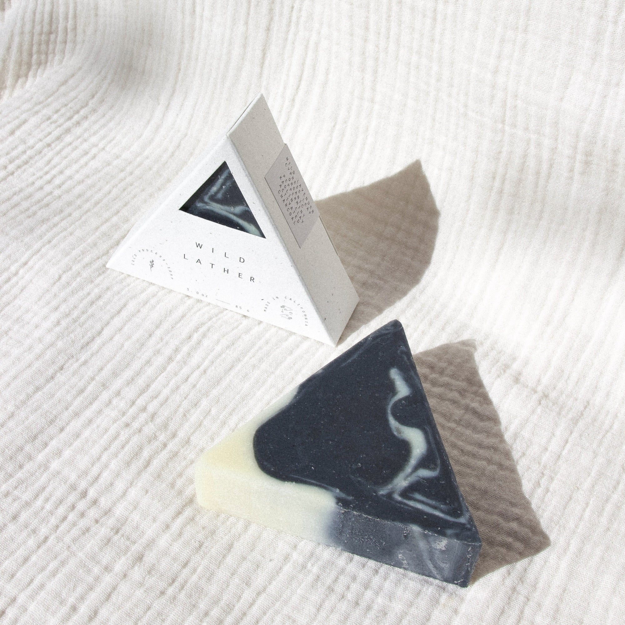 Activated charcoal triangle soap in speckled white triangle packaging against a textured white cloth