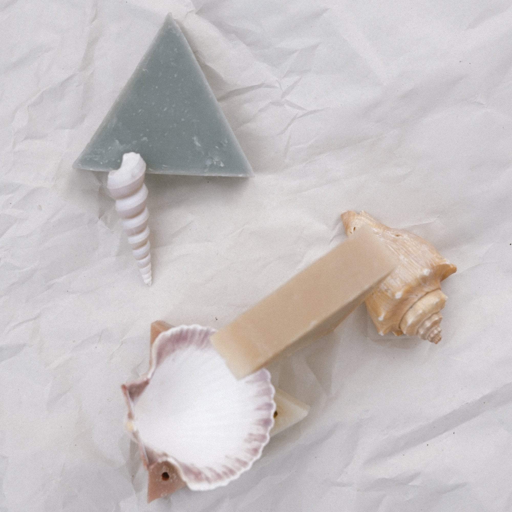Two triangle soaps with seashells against white crinkled paper