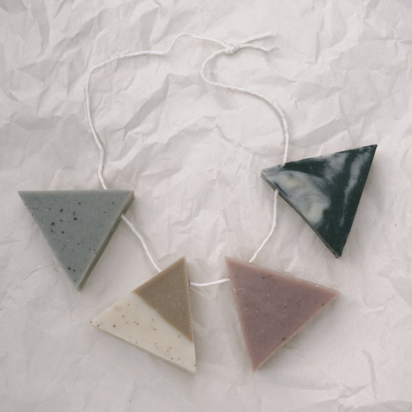 Four triangle soaps with string running through them like a necklace against crinkled white paper