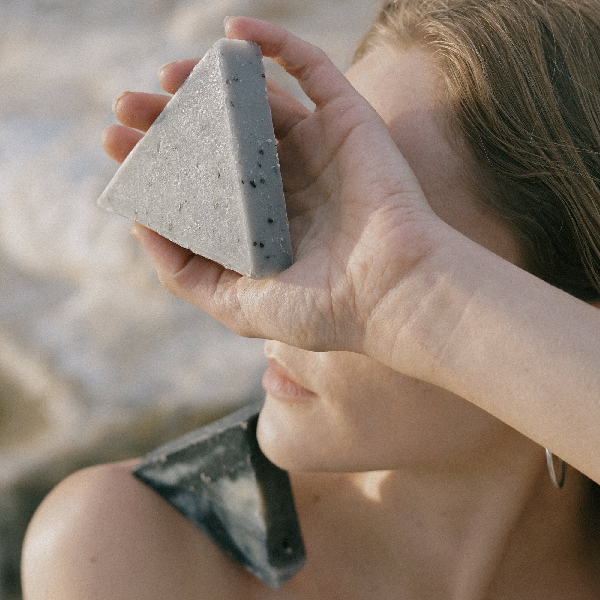 A closeup of a woman holding two triangle soaps at the beach