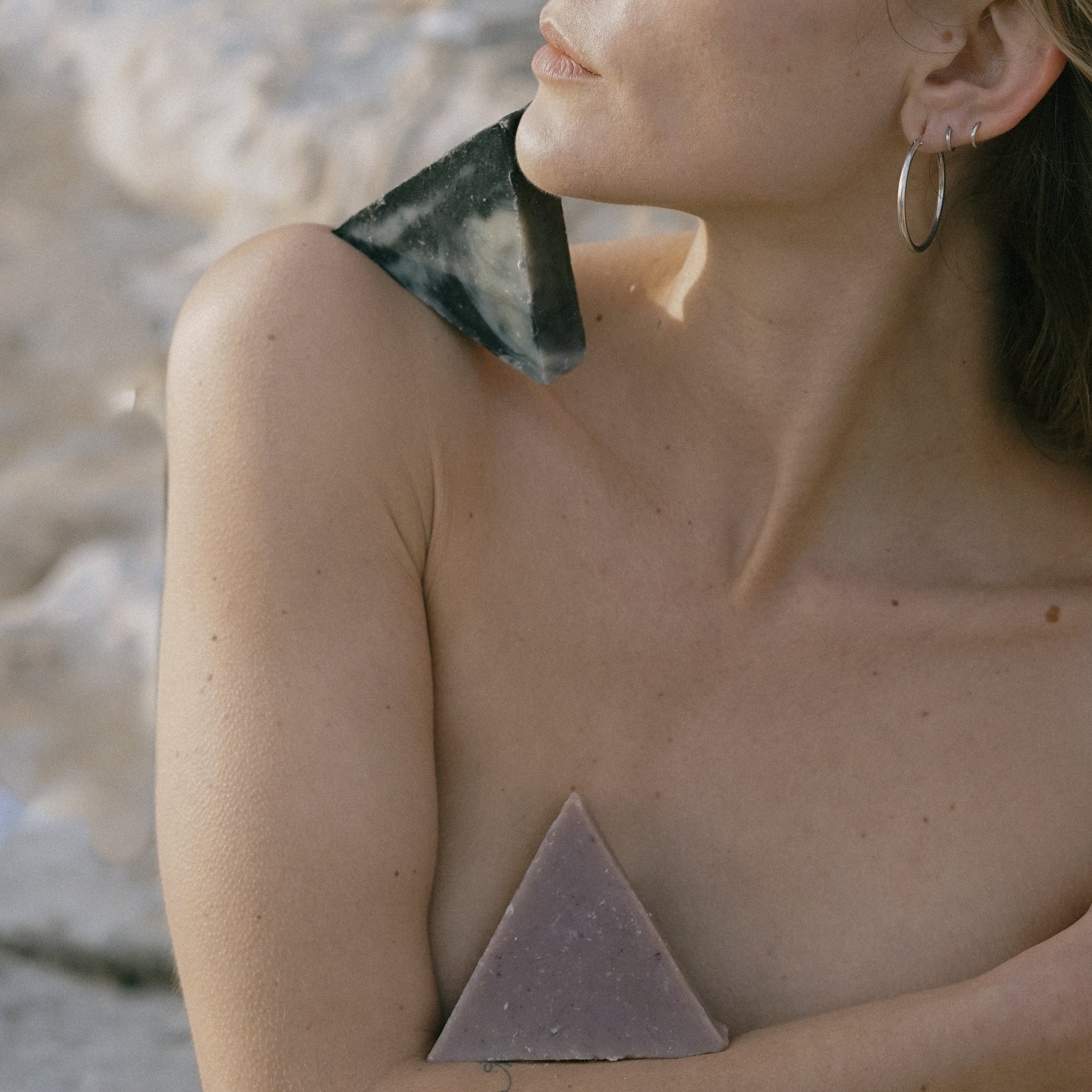 A closeup of a woman holding two triangle soaps at the beach