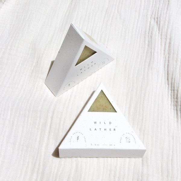 Two packaged triangle soaps against textured linen