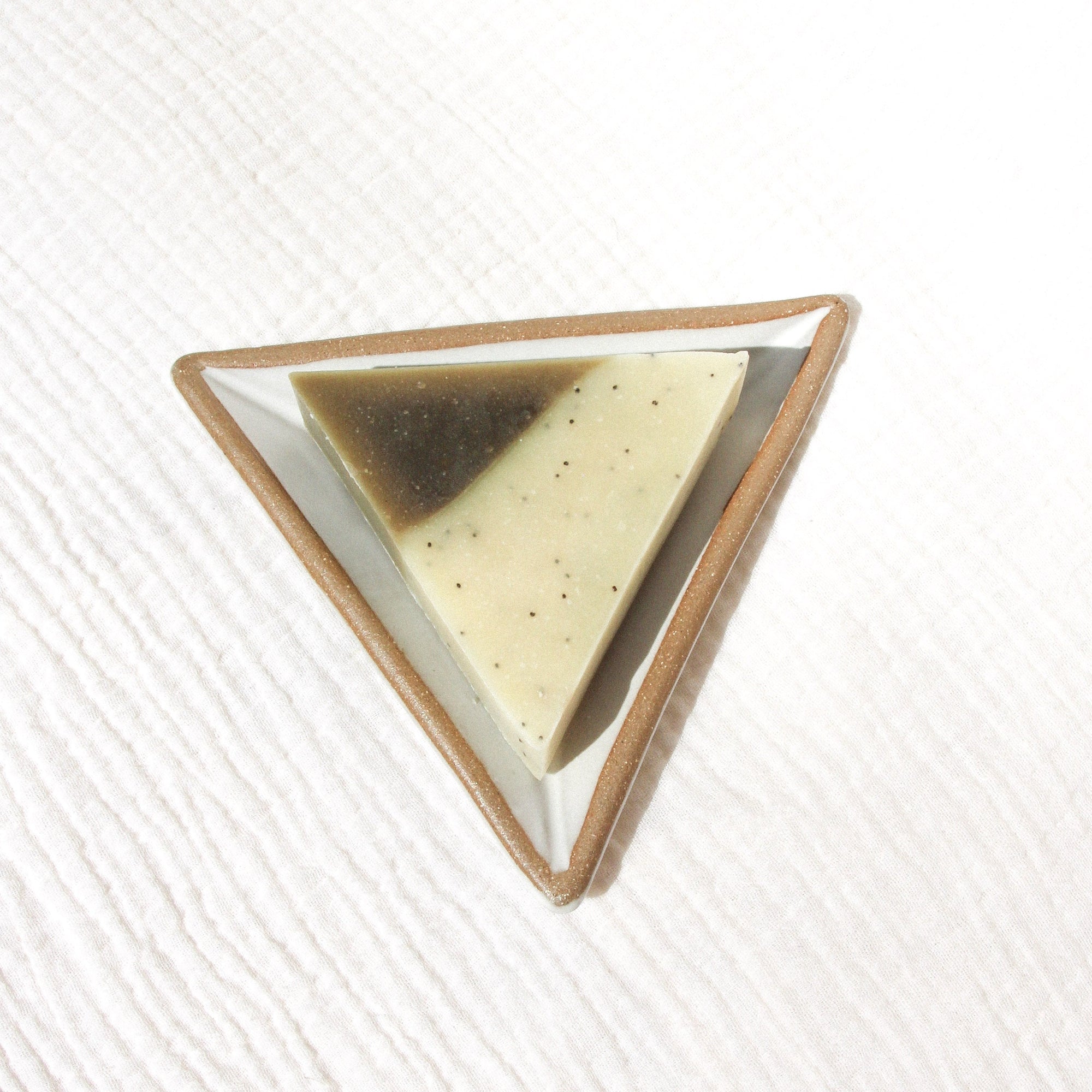 A triangle soap on a triangular soap dish against textured linen