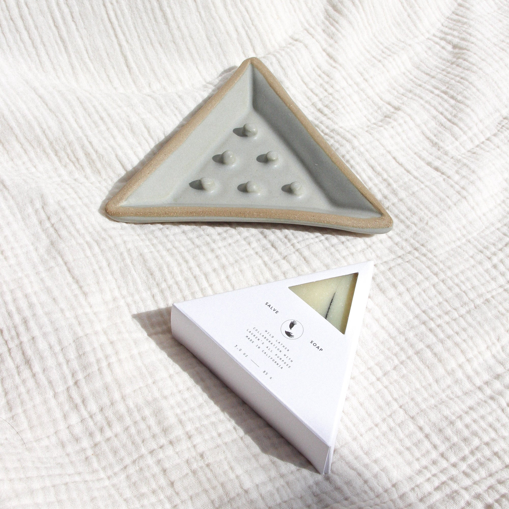 A triangular soap dish and packaged triangle soap against textured linen