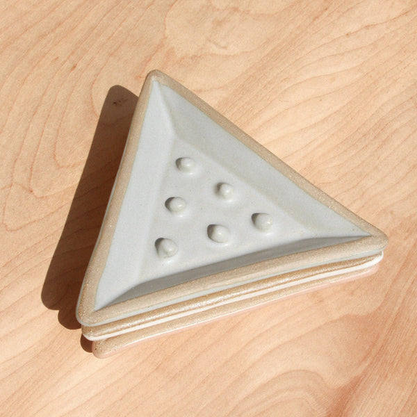 Three triangular ceramic soap dishes stacked on top of each other against wood grain