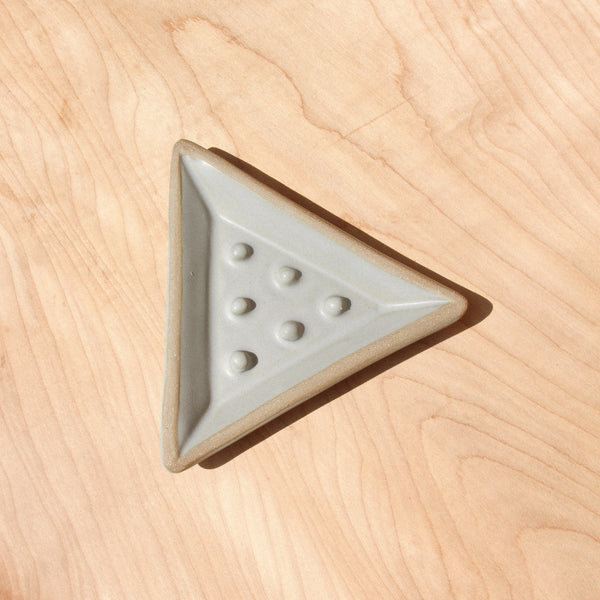 A ceramic triangular soap dish against wood grain