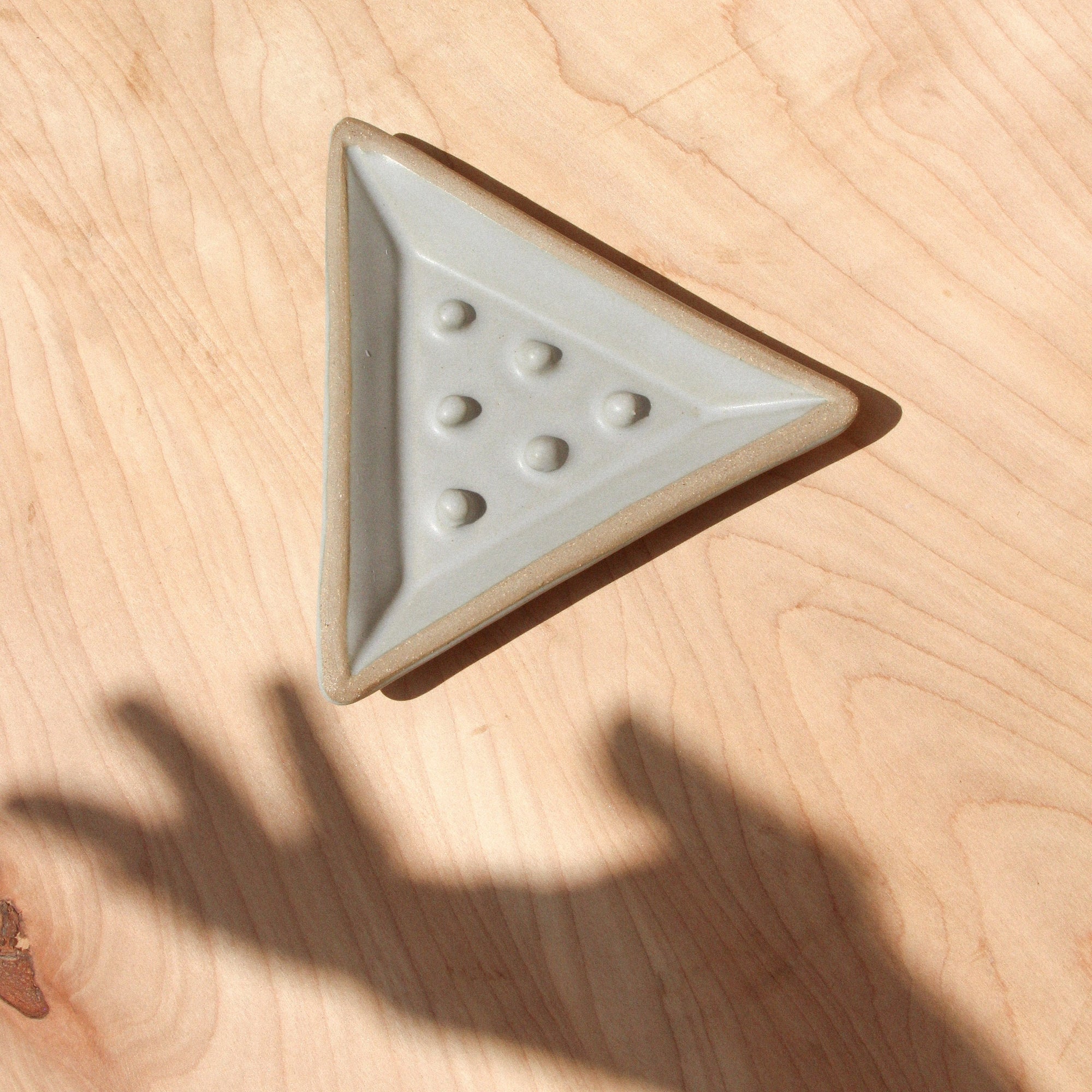 A ceramic triangular soap dish and shadow hand against wood grain