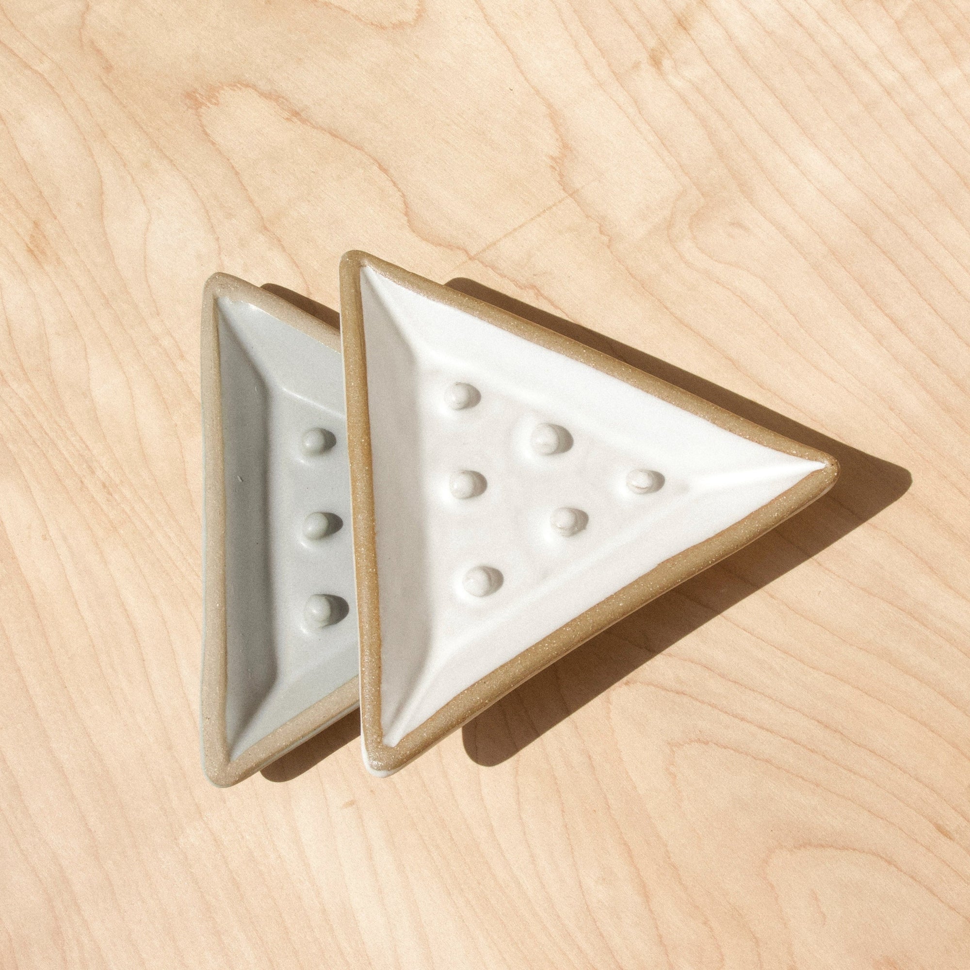 Two triangular ceramic soap dishes against wood grain