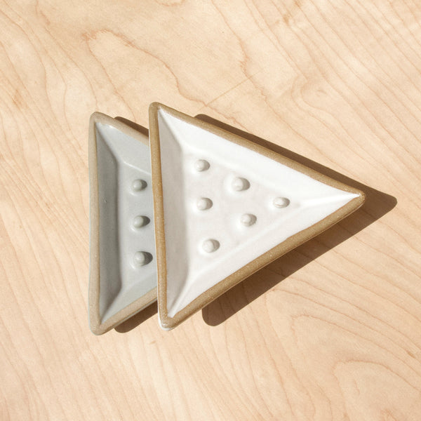 Two triangular ceramic soap dishes against wood grain