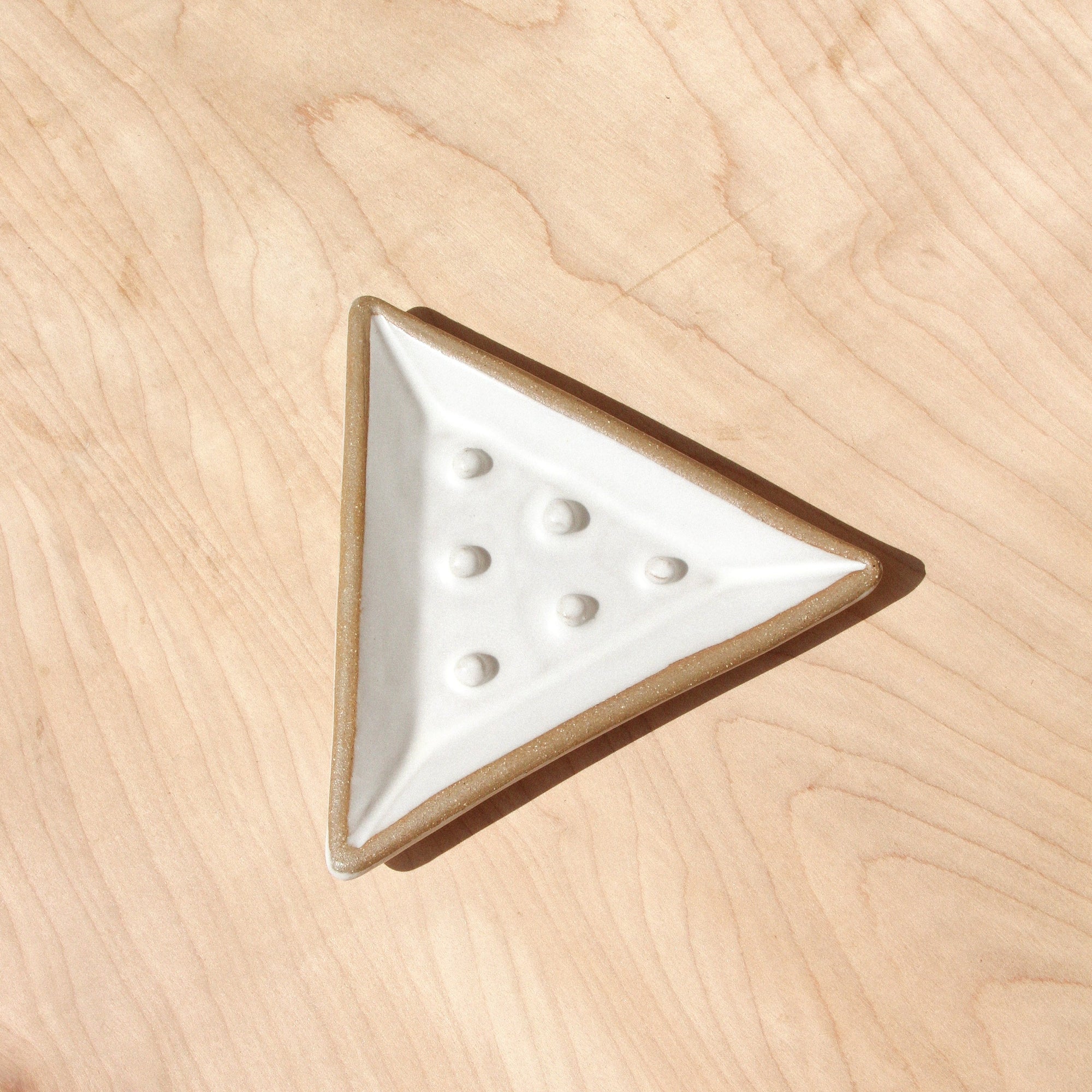 A white ceramic triangle soap dish against wood grain