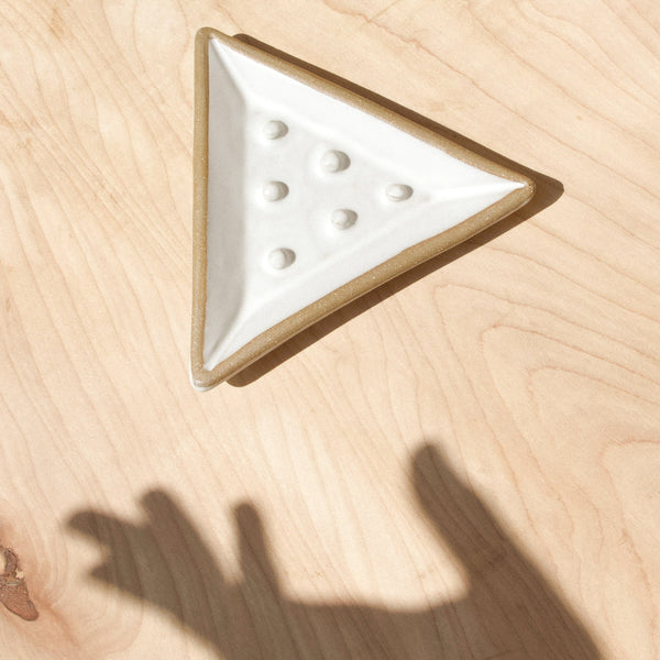 A white ceramic triangular soap dish and shadow hand against wood grain