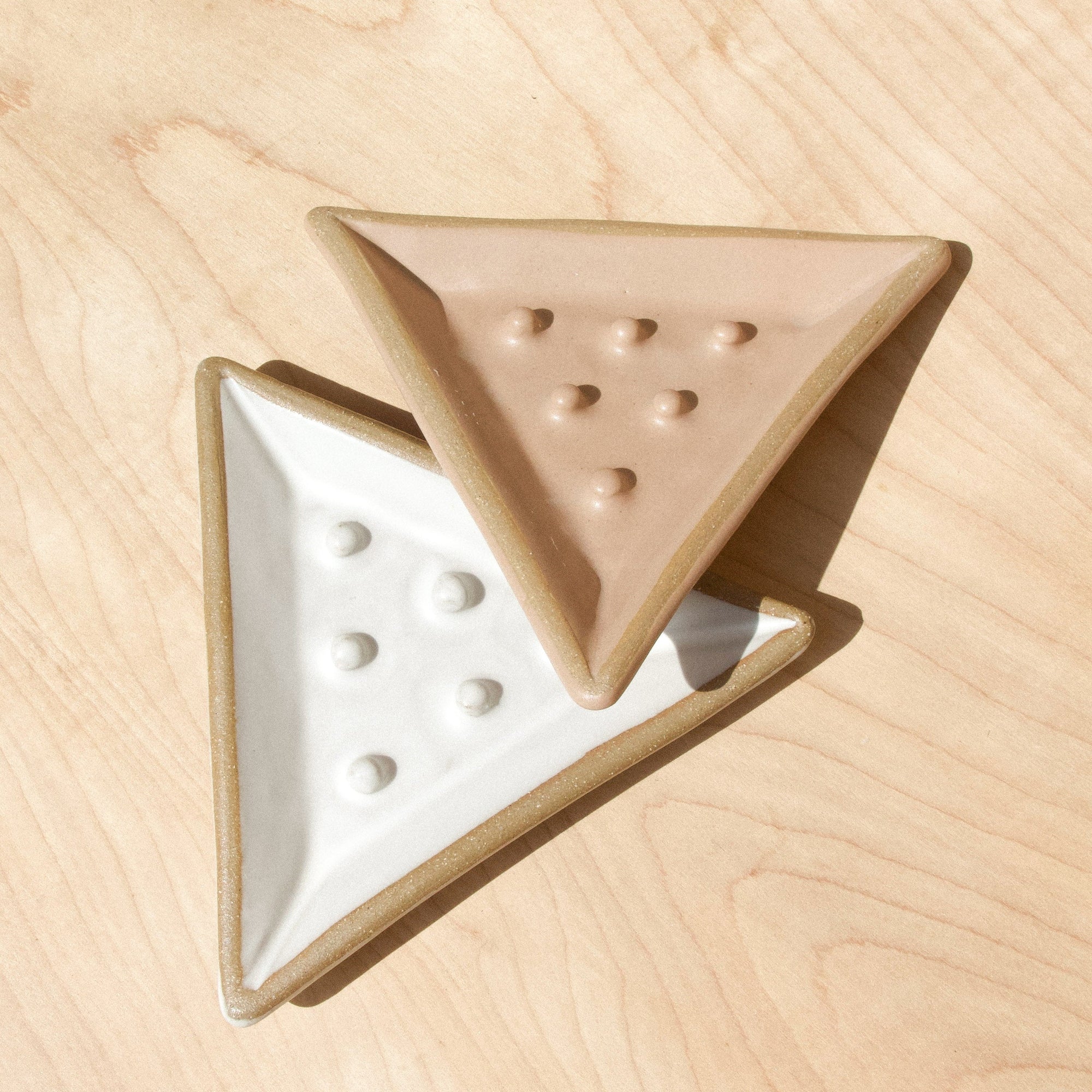Two triangular ceramic soap dishes against wood grain