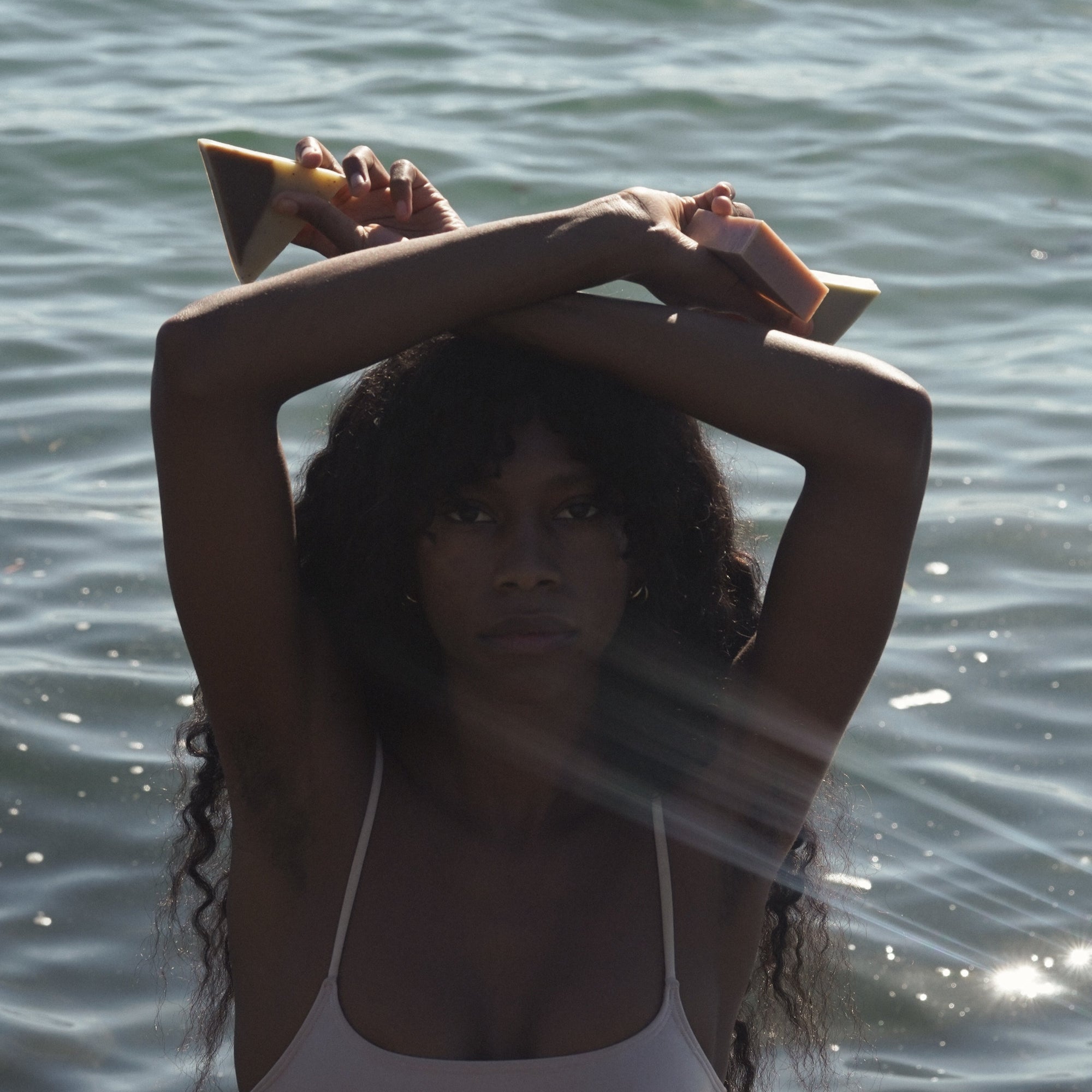 A woman holding three soaps above her head in front of the ocean
