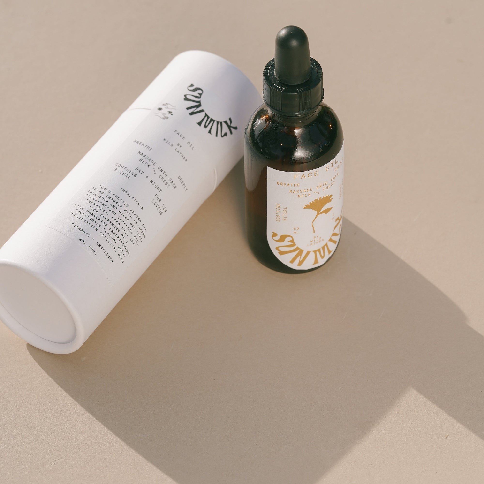 A bottle of Sun Milk Oil next to its white paper tube packaging on a beige surface with shadows