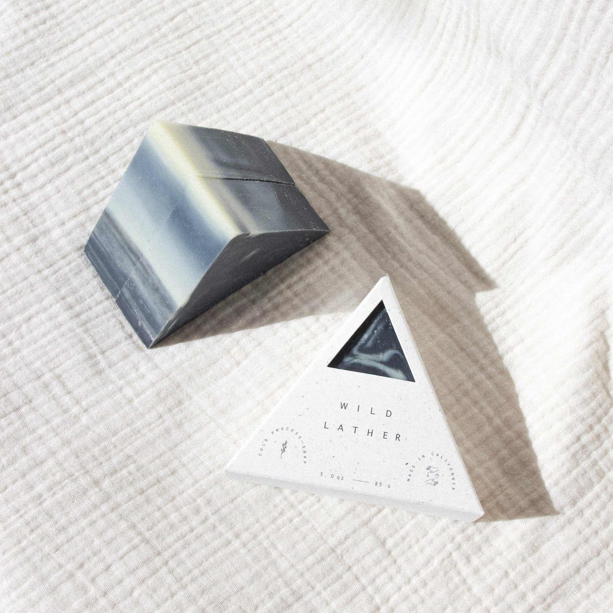 Activated charcoal triangle soap in speckled white triangle packaging against a textured white cloth