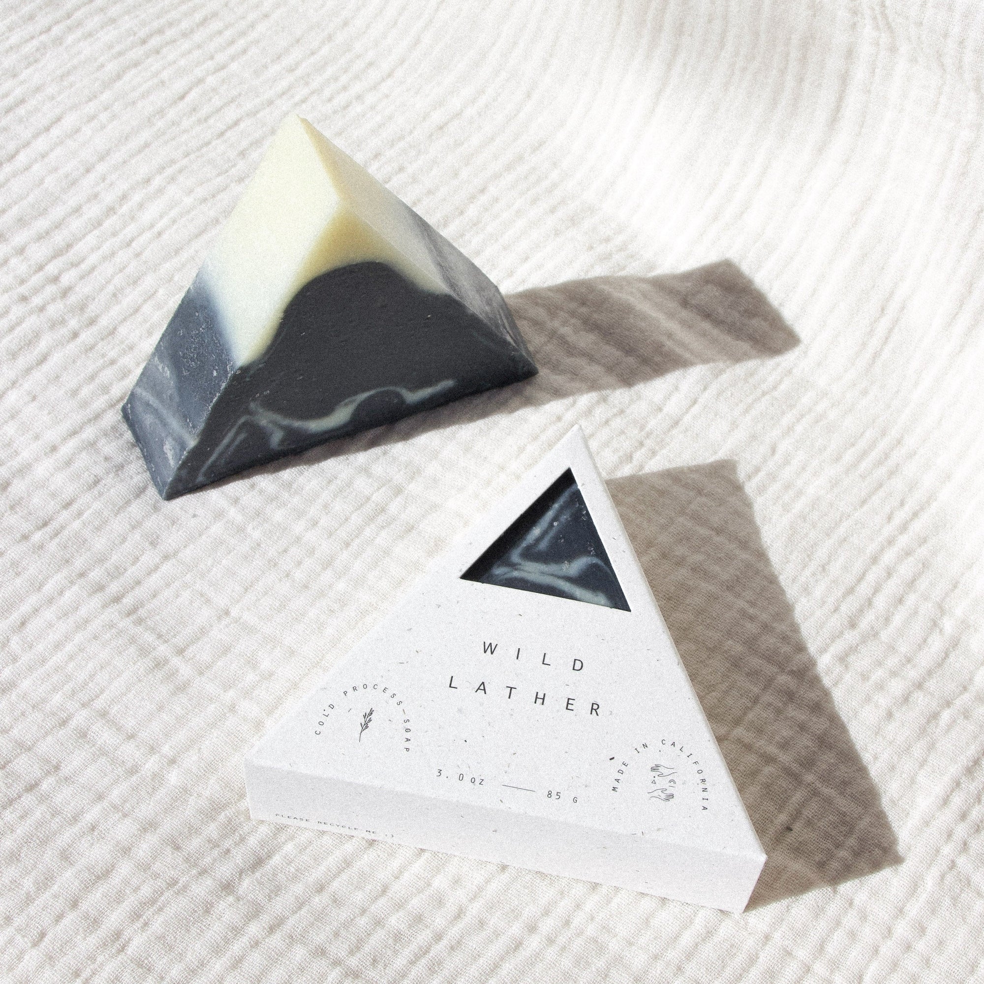 Activated charcoal triangle soap in speckled white triangle packaging against a textured white cloth