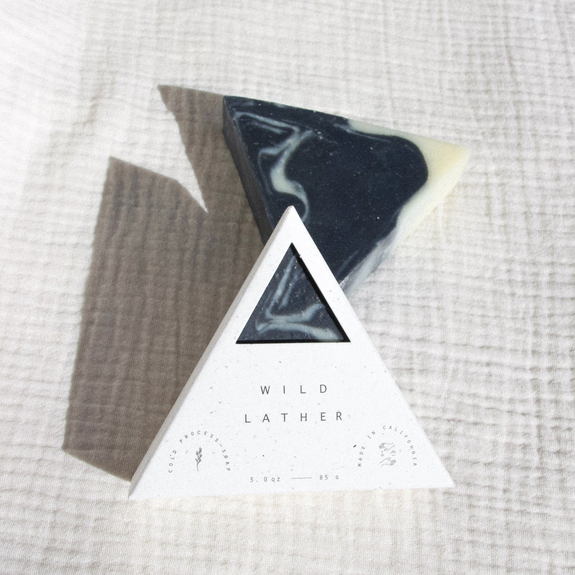 Activated charcoal triangle soap in speckled white triangle packaging against a textured white cloth