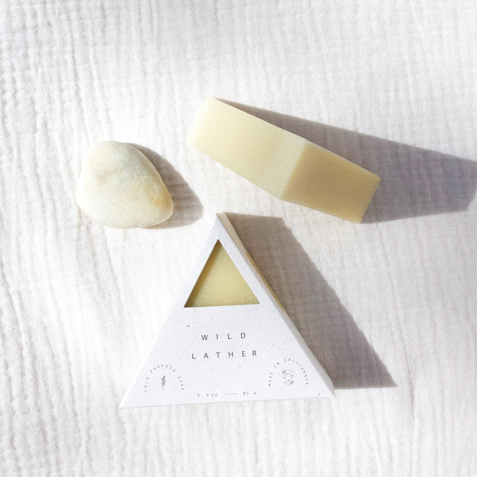 Two triangle soaps and a stone against a textured cream cloth
