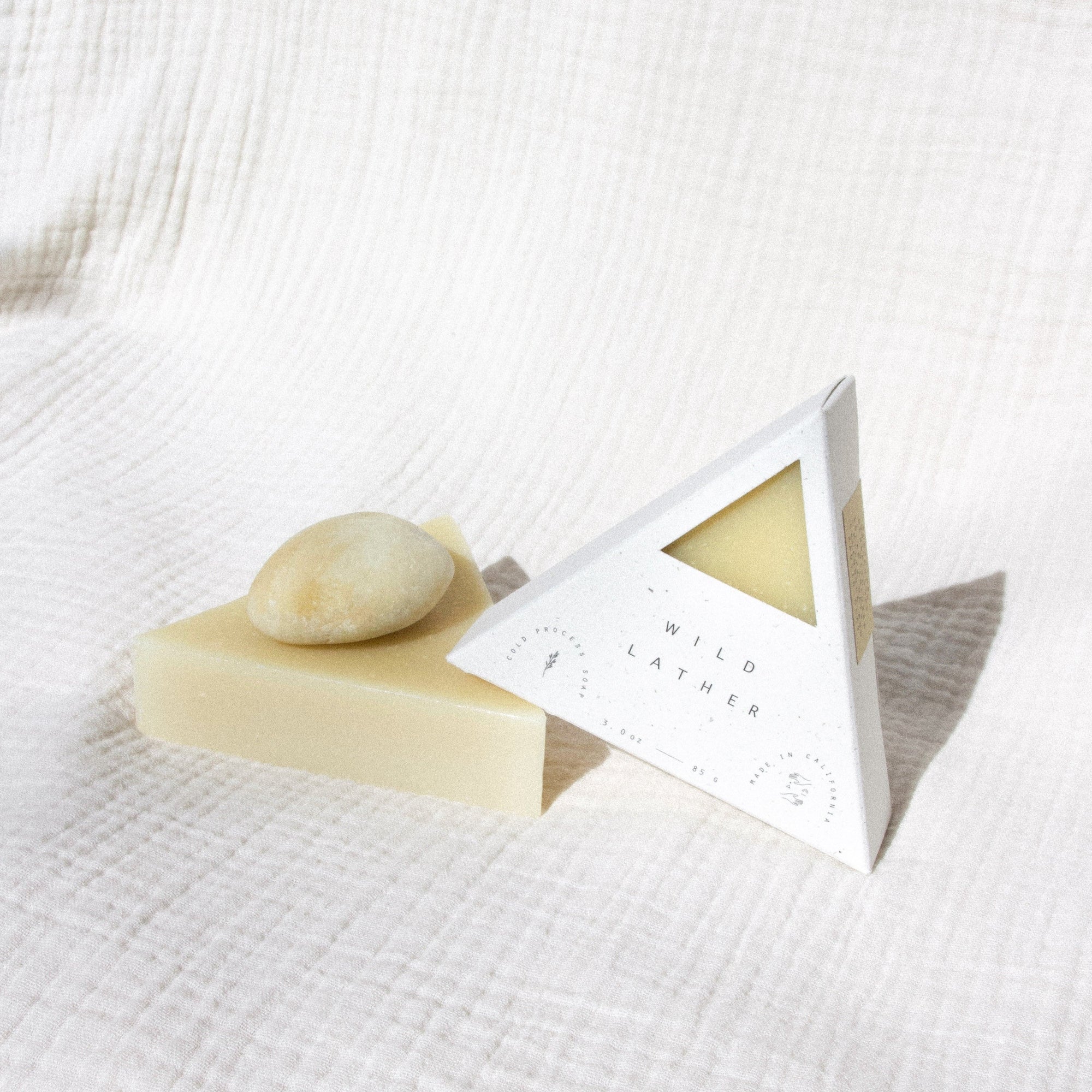 Two triangle soaps and a stone balancing against a textured cream cloth
