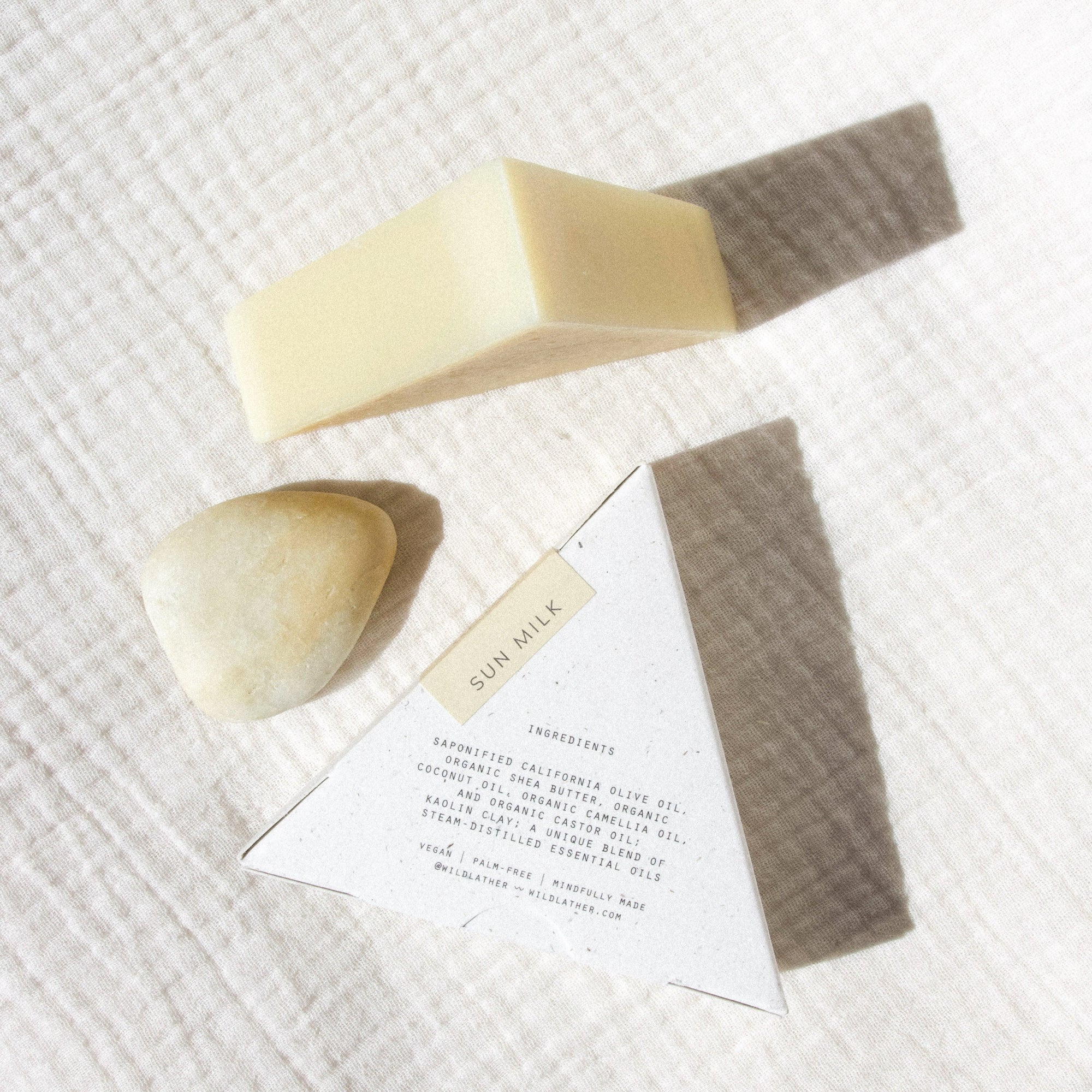 Two triangle soaps and a stone against a cream textured cloth