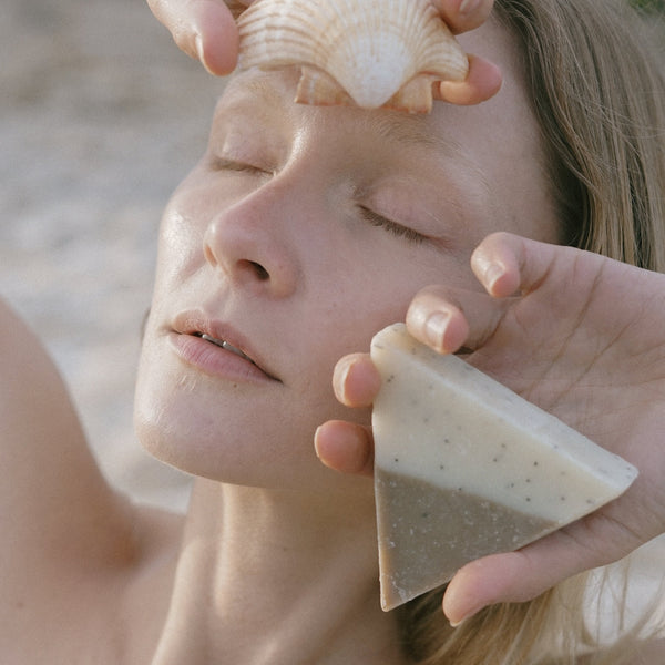 A woman at the beach holding a triangle soap and seashell in her hands