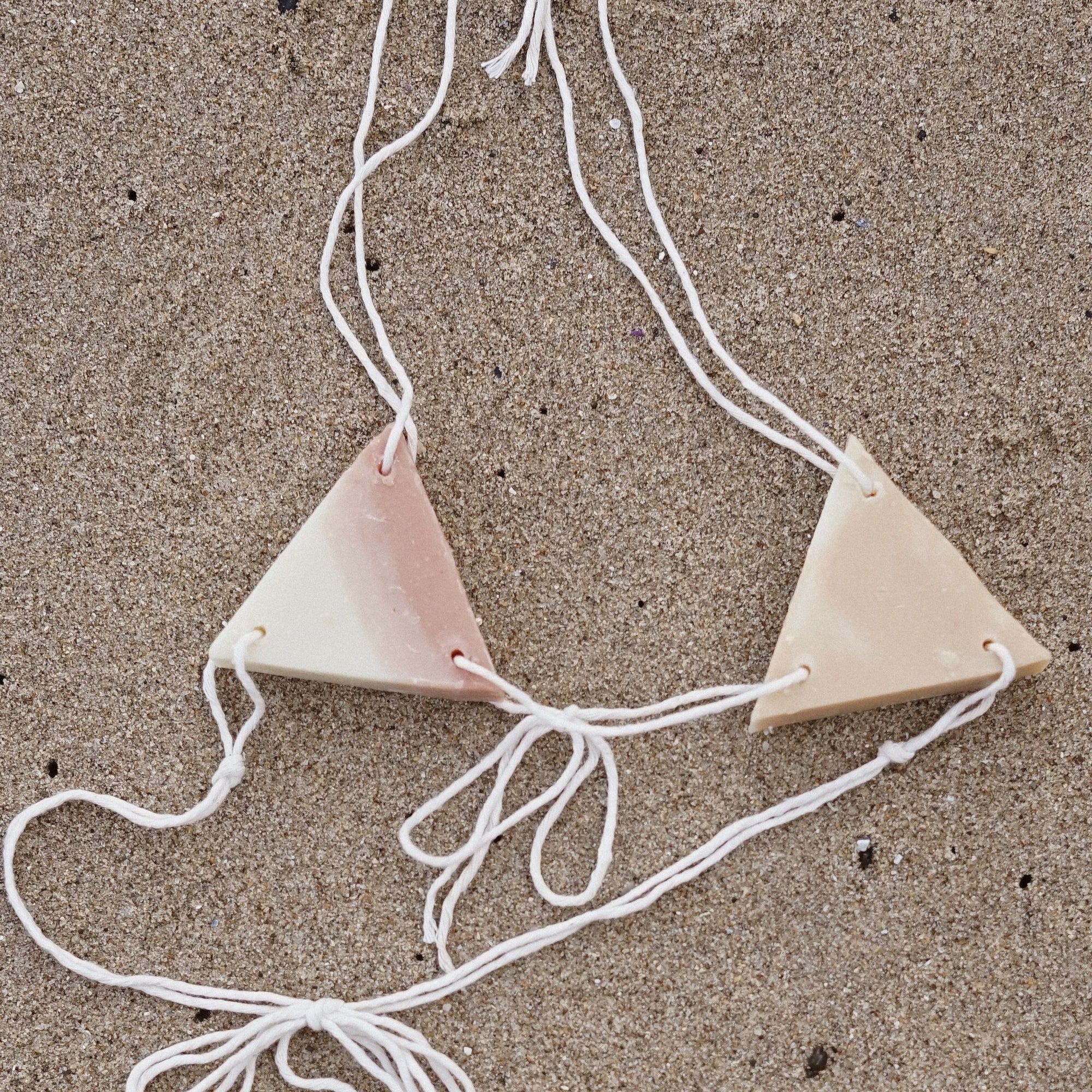 A bikini top against sand made of triangle soap and white string 