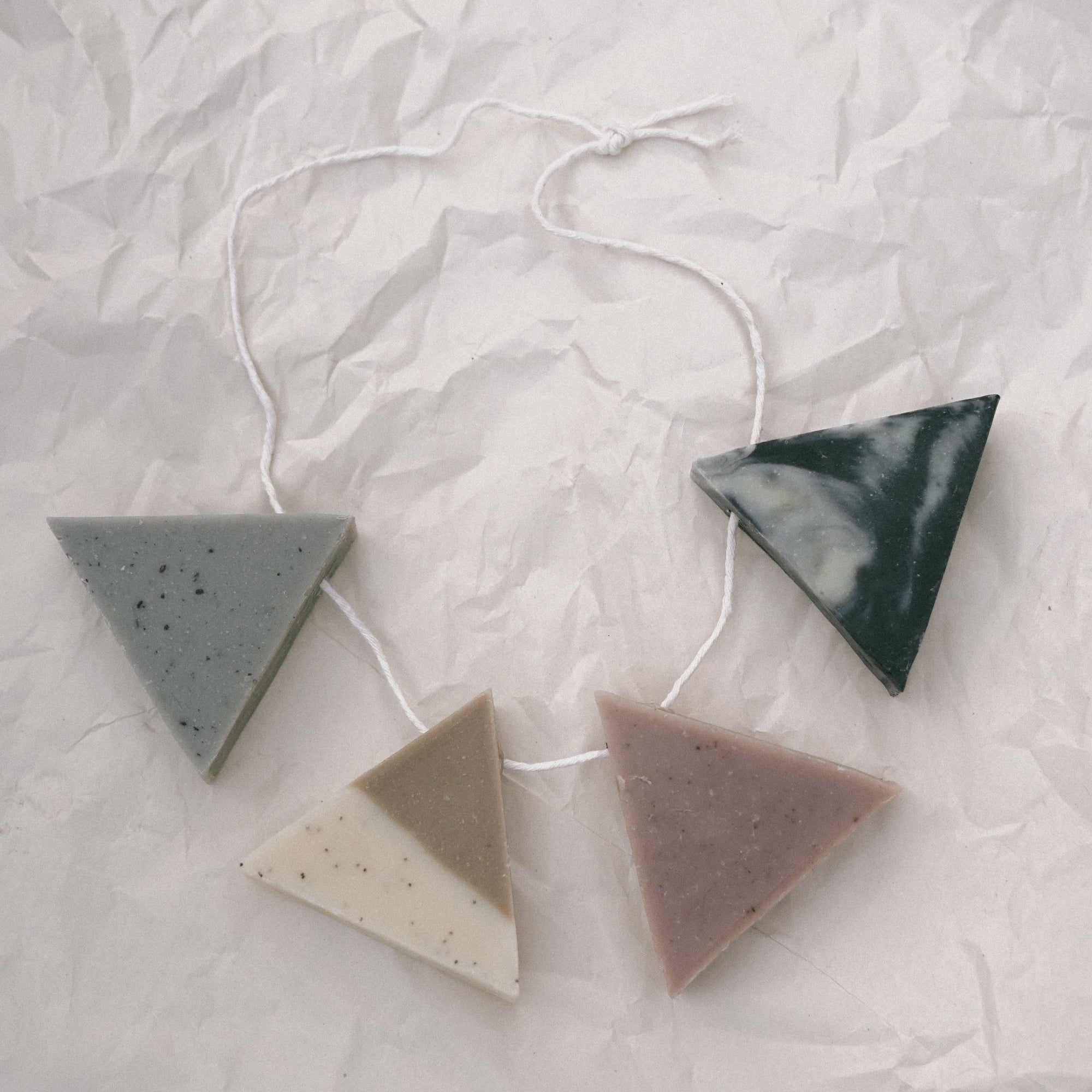A necklace of four triangle soaps against crinkled white paper