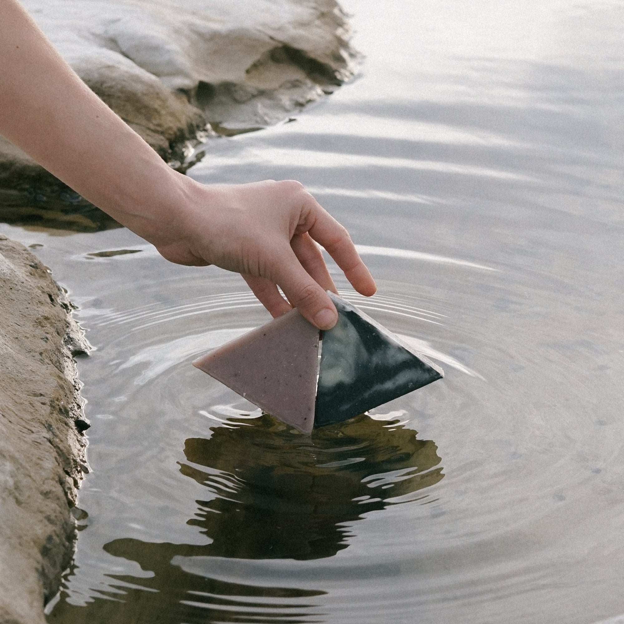 A woman's hand holding two triangle soaps slightly dipped in water