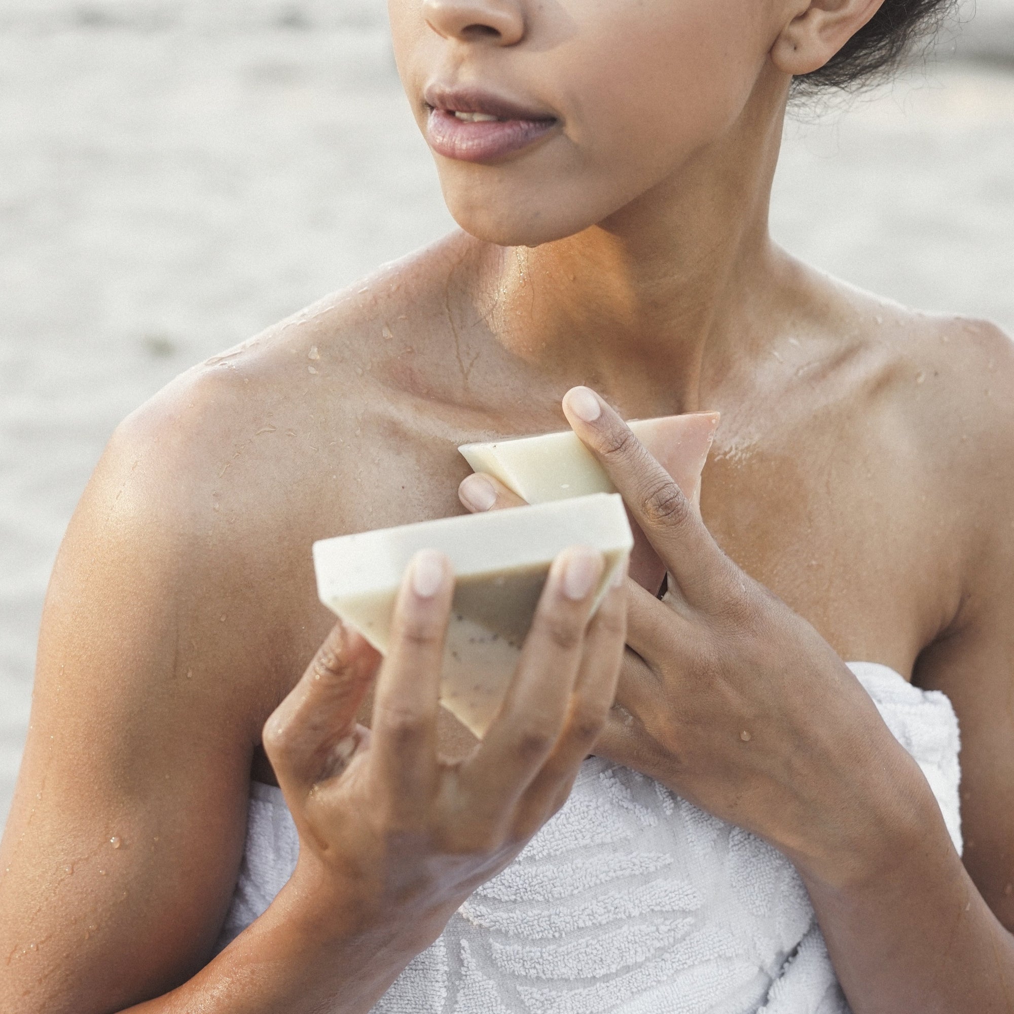 A woman wrapped in a white towel at the beach holding two triangle soaps 