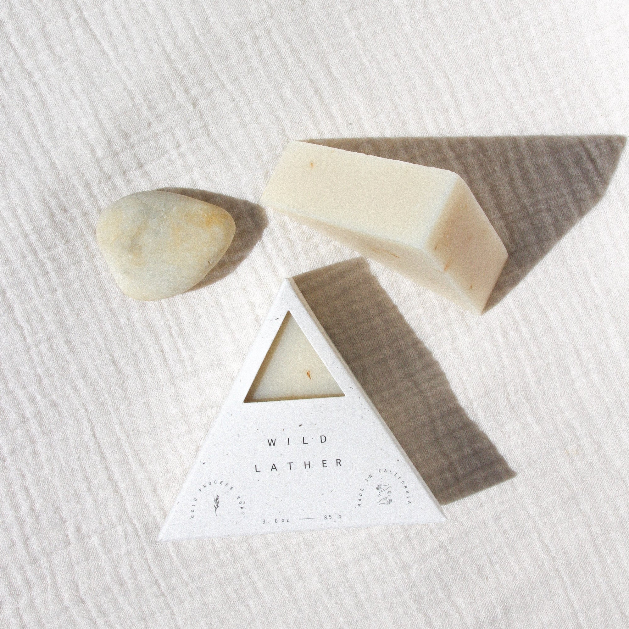 Two triangle soaps and a stone on a textured beige linen cloth