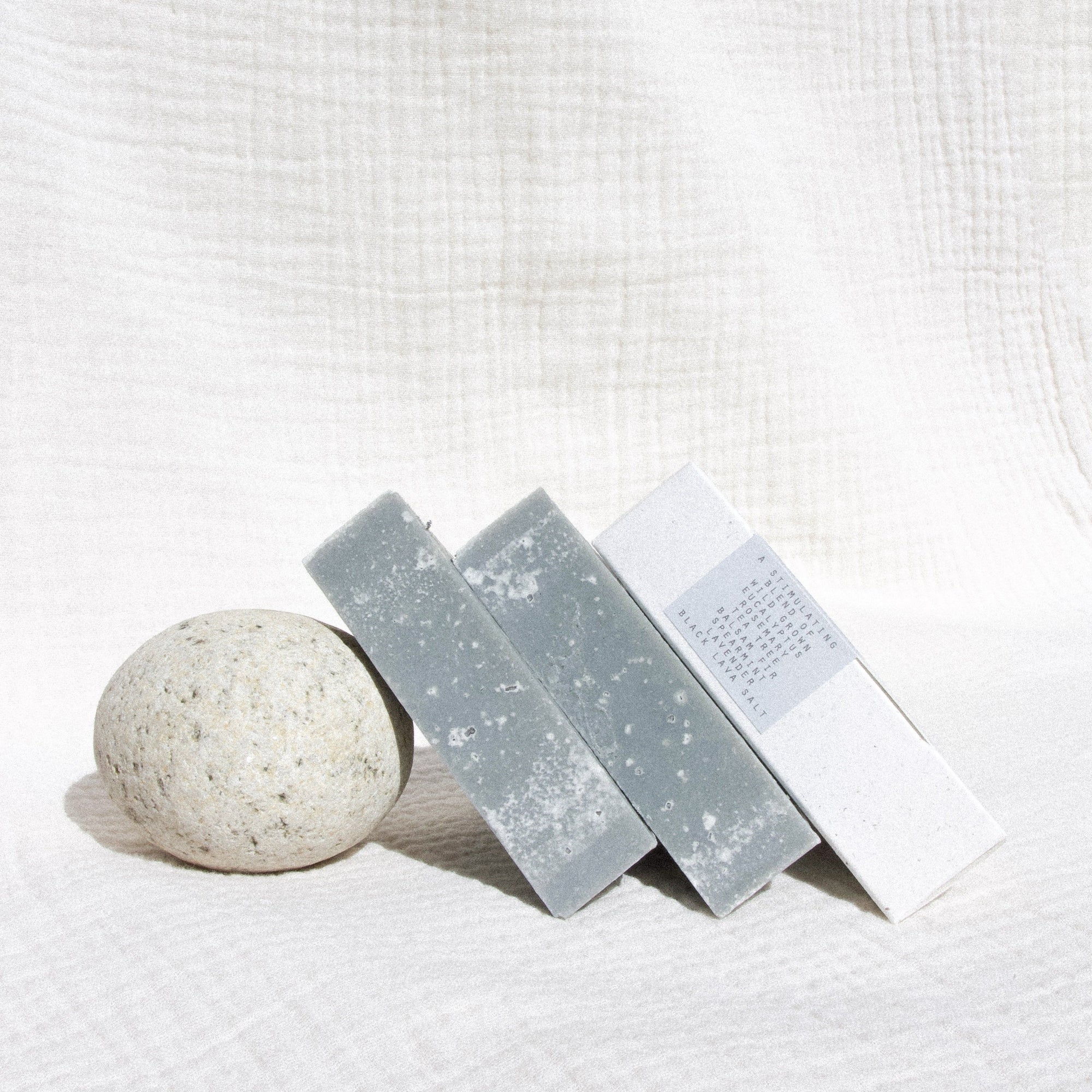 Three soap leaning against a round rock against textured linen